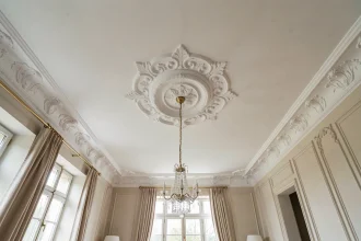 Plafond décoratif avec moulures en plâtre blanc et médaillon central dans un salon rénové au style classique français