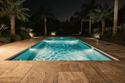 Piscine rectangulaire moderne illuminée de nuit par des LEDs sous-marines turquoise avec terrasse en travertin